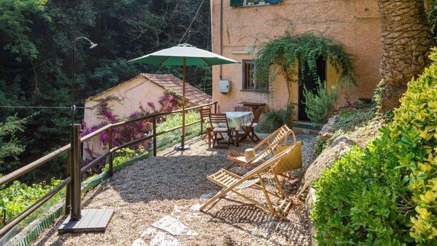 Un edificio rústico con balcón, mesas al aire libre y vistas a un bosque frondoso.
