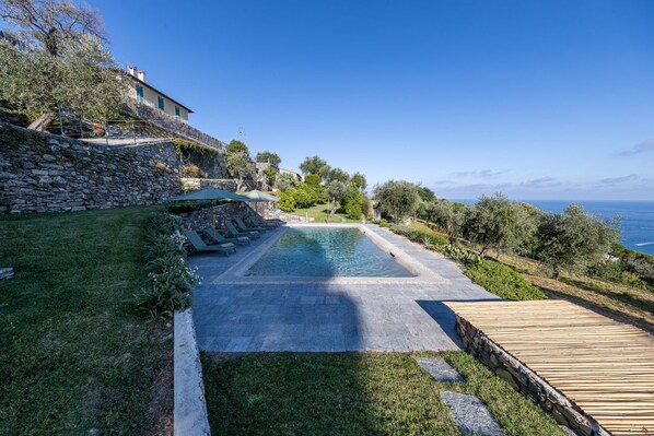 Una piscina con borde de piedra, cubierta de madera y pared de piedra con una escalera que lleva a un edificio.