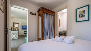 Une chambre d’hôtel avec un lit, un miroir dans la salle de bain, un téléviseur dans la pièce adjacente et un tableau encadré au mur.