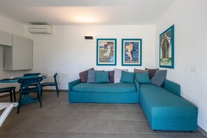 Un espacio de sala con un sofá color turquesa, una mesa de comedor con sillas y tres carteles enmarcados en la pared.