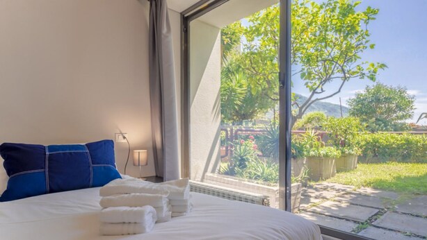 A bedroom with a large window, a bed with white linens, and a view of greenery outside. - HAPPY HOLIDAY - Open space with sea view (Camogli)
