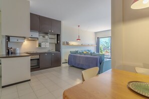 A modern kitchen with built-in appliances, a dining area with a wooden table, and a bed with a blue cover.