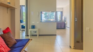 A modern hotel room with a sofa, a small table, a window with a view, and a door leading to another room. - HAPPY HOLIDAY - Open space with sea view (Camogli)