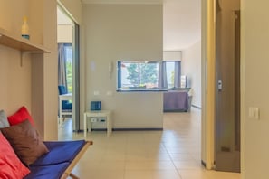Une chambre d’hôtel moderne, équipée d’un canapé, d’une petite table, d ’une fenêtre avec vue et d’une porte donnant sur une autre pièce.