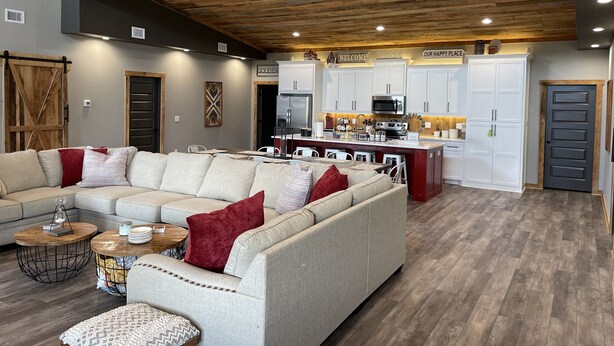 Una sala de estar moderna con un sofá modular, techo de madera y una cocina con armarios y electrodomésticos blancos.