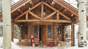 Eine Blockhütte mit einer Holzveranda, einer Tür und einem Fenster. Es schneit draußen.