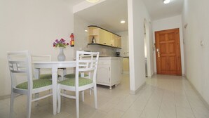 A dining area with a white table and chairs, a vase with flowers, and a kitchen in the background.
