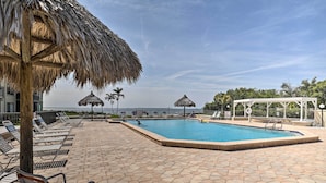 Un espace piscine avec des chaises longues et un parasol en chaume, une piscine et une vue sur la mer.