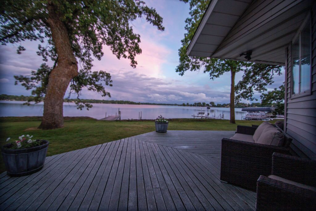 Une terrasse en bois avec des meubles d’extérieur, un grand arbre et une vue sur un lac.