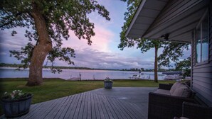 Un terrazzo in legno con mobili da esterno, un albero grande e vista su un lago.