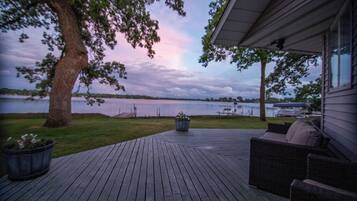 Une terrasse en bois avec des meubles d’extérieur, un grand arbre et une vue sur un lac.