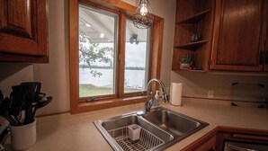 Una cucina con lavello in acciaio inossidabile, mobili in legno, una finestra vista lago e un lampadario.