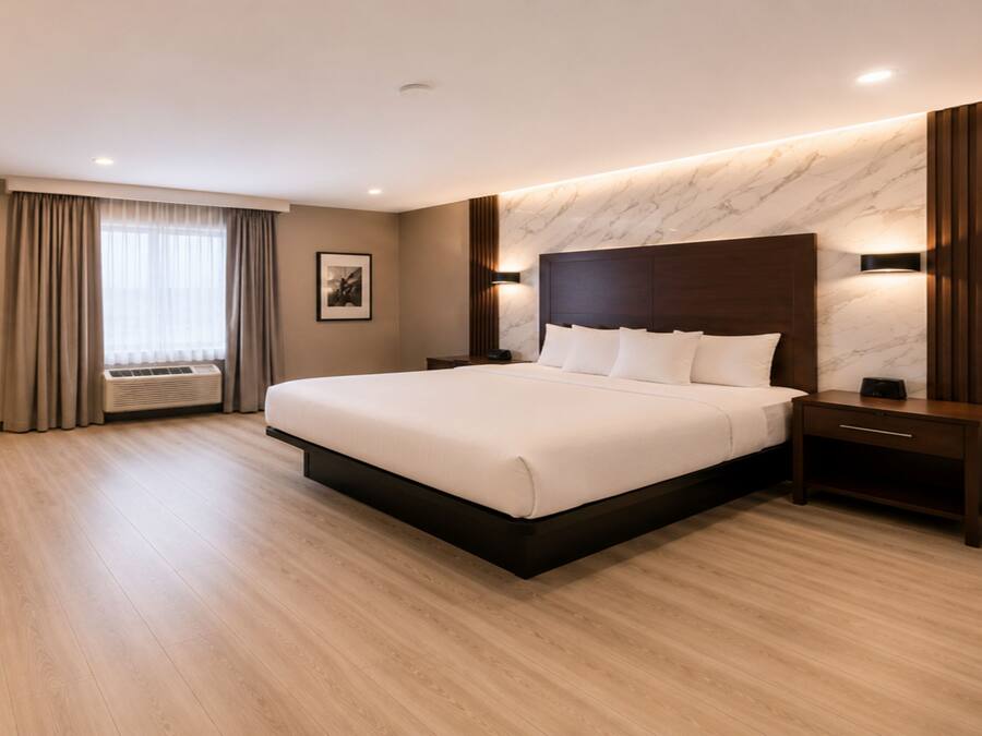 Habitación de hotel con una cama grande, una mesita de noche, una lámpara de pared, una ventana con cortinas y un radiador.