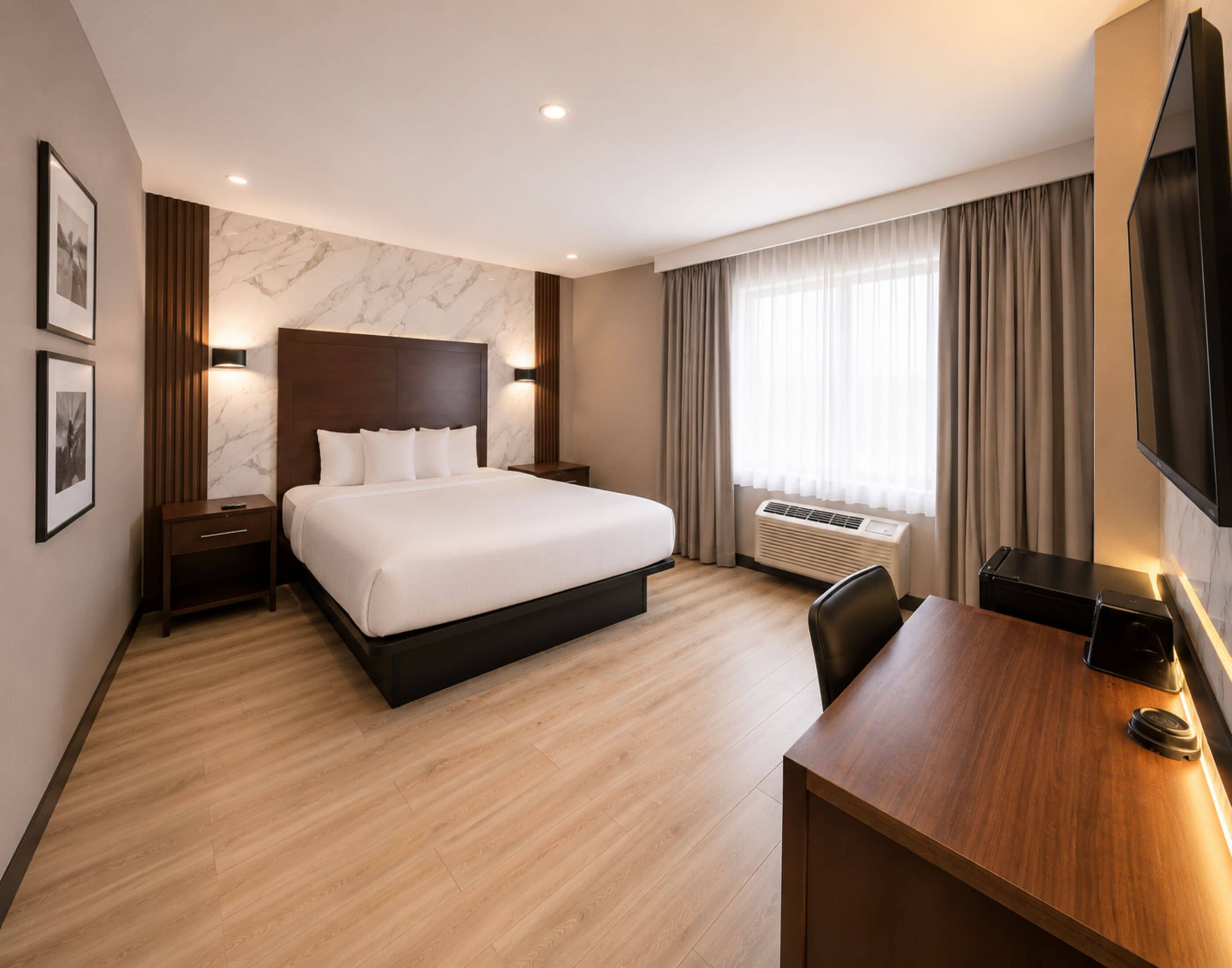 Habitación de hotel con una cama grande, un escritorio, un televisor de pantalla plana, aire acondicionado instalado en la pared y cuadros enmarcados.