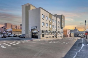 Hotel com fachada moderna, entrada visível e vista da rua com carros e faixa de pedestres.