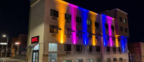 Un hôtel à plusieurs étages, doté d’une enseigne et de fenêtres illuminées, situé à un angle de rue.