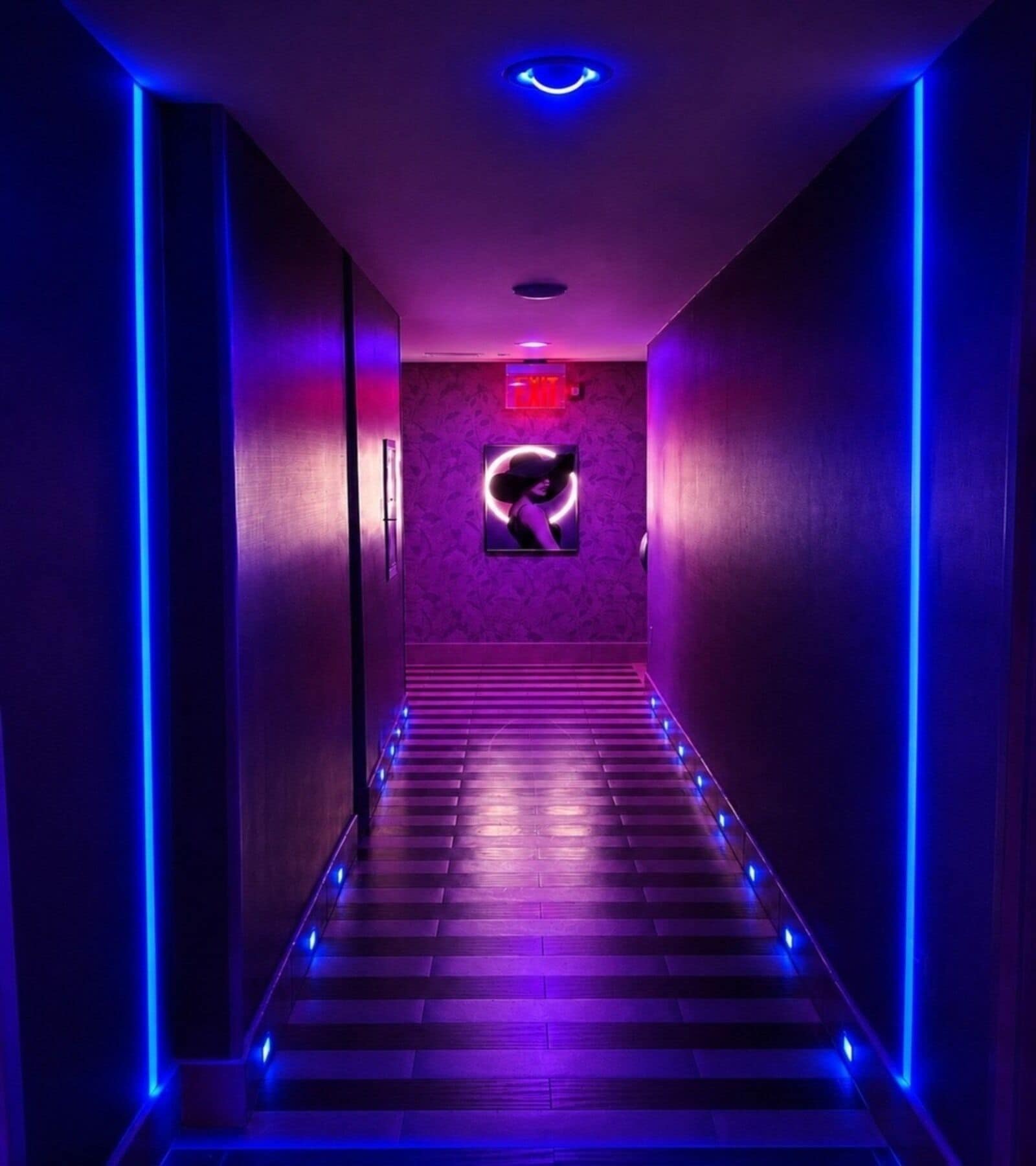 A hallway with a patterned wall, a framed picture, and a neon sign.