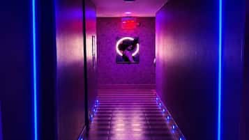 A hallway with a patterned wall, a framed picture, and a neon sign.
