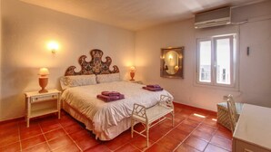 A bedroom with a bed, two bedside tables with lamps, a chair, a window, and an air conditioning unit. - 1079 - FRONTLINE PUERTO BANUS APARTMENT (Marbella)