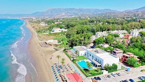 Vista aérea de una zona costera con playa, piscina y una combinación de edificios residenciales y comerciales.
