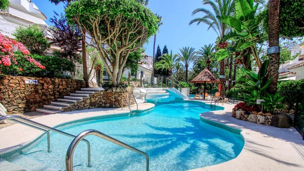Una piscina con pared de piedra, barandillas de metal y escalones que bajan al agua.