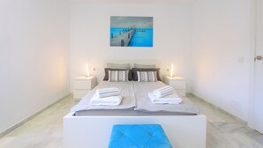 Un dormitorio moderno con una cama grande, dos mesitas de noche, un cuadro de un muelle y vistas al mar.
