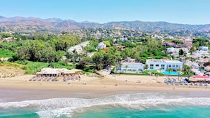 Un pueblo costero con playa, zona de piscina y vistas a montañas al fondo.