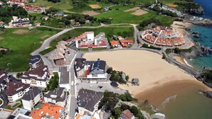 Vista aérea de un pueblo costero con playa de arena, un complejo de edificios centrales y zonas residenciales circundantes.