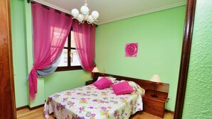 Un dormitorio con una colcha estampada, cabecera de madera, dos lámparas de noche y una ventana con cortinas rosadas.