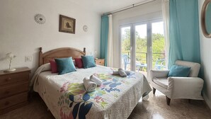 A bedroom with a bed, a nightstand, a chair, and a window with curtains. - Apto con jardín compartido - Villa Cancillo 6802 (Noja)
