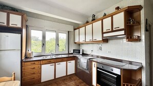 A kitchen with wooden cabinets, a microwave, a stove, and a sink. - Apto con jardín compartido - Villa Cancillo 6802 (Noja)