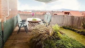 Una terraza en la azotea con una mesa y sillas, rodeada de vegetación y vistas a la ciudad.