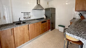 Una cocina con paredes de azulejos blancos, una campana extractora de acero inoxidable, un refrigerador y armarios de madera.