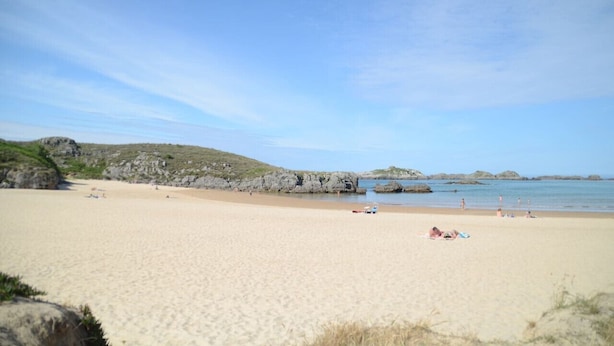Una playa arenosa con afloramientos rocosos y agua tranquila.