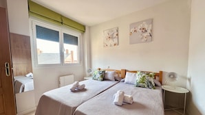 Una habitación de hotel con dos camas, una ventana con persianas, una mesita de noche con lámpara y una obra de arte en la pared.