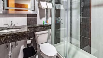A modern bathroom with a granite countertop sink, a white toilet, and a glass-enclosed shower area.