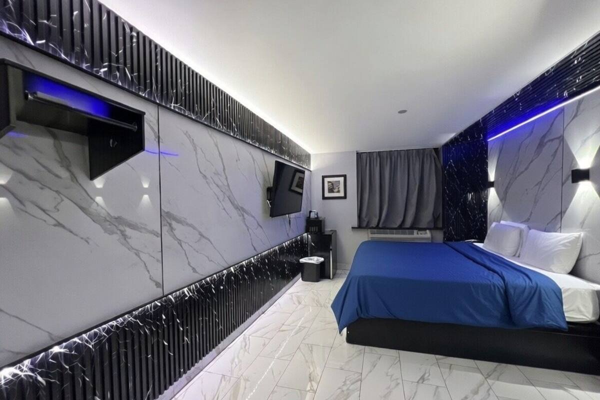 A modern bedroom with a large bed, a flat-screen TV mounted on the wall, and a built-in sound system.