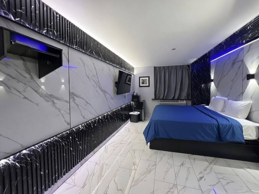 A modern bedroom with a large bed, a flat-screen TV mounted on the wall, and a built-in sound system.
