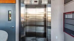 Un ascensor con pantalla digital, un botón de alarma de incendios y un panel de control en la pared.