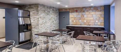 A modern kitchen with a stone wall backsplash, stainless steel appliances, and a seating area with metal chairs and tables.