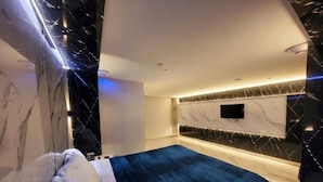 Un dormitorio moderno con cama, paredes de mármol y televisor de pantalla plana montado en la pared.