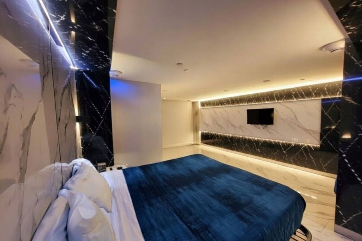 A modern bedroom with a bed, marble walls, and a flat-screen TV mounted on the wall.