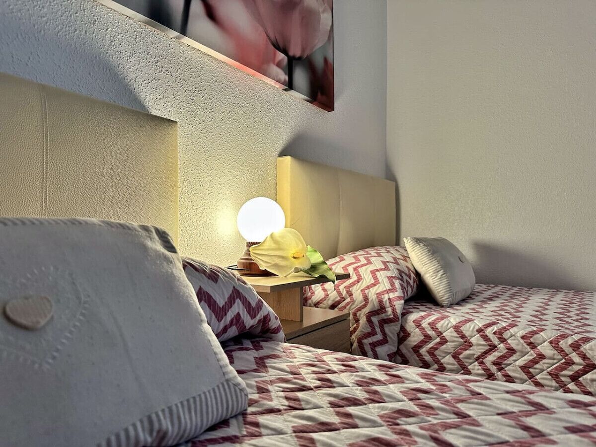 A bedroom with two beds, a nightstand with a lamp, and a wall-mounted shelf.