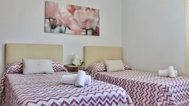 Ein Hotelzimmer mit zwei Betten, jeweils mit einem gemusterten Bettbezug und passenden Kissen. Darüber hängt ein Blumenbild an der Wand.