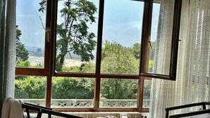 Una stanza con un'ampia finestra, un tavolo, due sedie e vista su vegetazione e un paesaggio lontano.