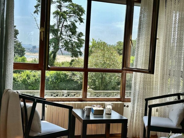 A room with a large window, a table, two chairs, and a view of greenery and a distant landscape.