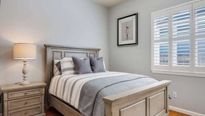 A bedroom with a bed, nightstand, lamp, and a window with blinds. - Wine Country Harvest Vacation Home (Santa Rosa)