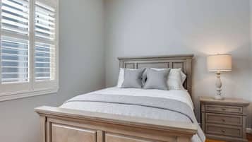 A bedroom with a bed, nightstand, lamp, and window with blinds.