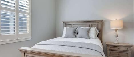 A bedroom with a bed, nightstand, lamp, and window with blinds.