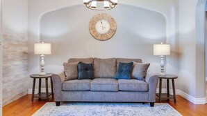 A living room with a grey sofa, two side tables with lamps, a chandelier, and a wall clock. - Wine Country Harvest Vacation Home (Santa Rosa)